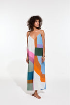 Une femme porte une longue robe géométrique. la robe est dans les tons bleu ciel, vert, rose, blanc et orange avec des lignes ou des carreaux. 